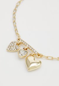 Collana in oro con tre ciondoli: un cuore d'oro, un cuore con cristalli trasparenti e un cuore di pietra trasparente con accenti in argento.