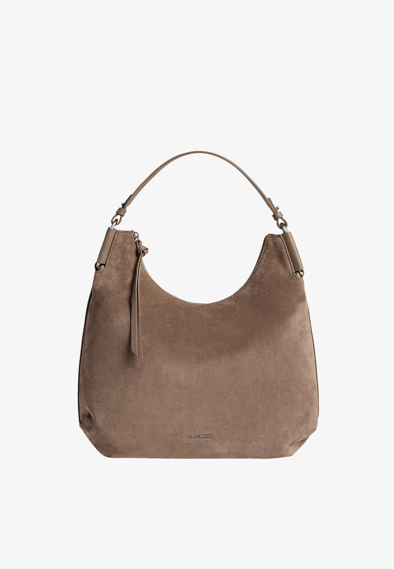 Beżowa torebka z zamszu o zaokrąglonym kształcie, z krótkim paskiem i dyskretnym logo na dole. Gładka tekstura o minimalistycznym designie.