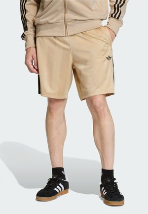 Pantalones cortos deportivos beige con acabado brillante, con franjas laterales negras y un logotipo bordado. Hechos de un material ligero y suave.