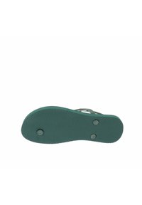 La suela de goma verde presenta un agarre texturizado, una forma redondeada y dos acentos circulares. Diseñada para ofrecer tracción y durabilidad.