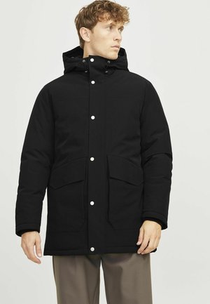 Čierna bunda s kapucňou a zipsom, ktorá má dve veľké vrecká, biele cvoky a matný, textúrovaný povrch.