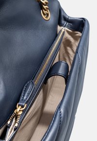 Borsa a mano in pelle blu navy con una texture liscia, dotata di zip e dettagli in catena dorata. L'interno è foderato in beige chiaro e presenta una tasca con zip.