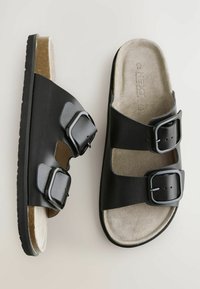Schwarze Ledersandalen mit zwei verstellbaren Riemen, strukturiertem Fußbett, flacher Sohle und glänzenden schwarzen Schnallen. Heller, beige Fußbett mit weicher Textur.