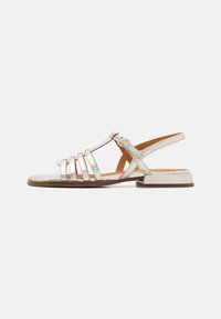 Sølvmessings metalliske stroppesandaler med lav hæl, med brede stropper, justerbar ankelspenne, og et stilrent, minimalistisk design.