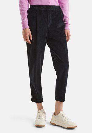 Pantaloni in corduroy neri con vestibilità rilassata, dotati di una vita arricciata e orli arrotolati, abbinati a sneakers bianche e beige.