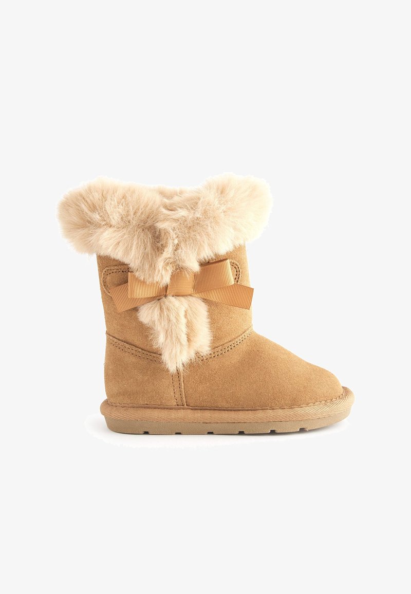 Bottines en nubuck beige avec un col en fourrure moelleux, un pompon en fourrure décoratif et un nœud en satin sur le côté. Semelle plate en caoutchouc.