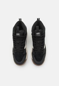 Zapatillas altas negras con paneles de ante y malla, con cordones negros, una franja blanca y una suela de goma marrón. Logo de VANS en la lengüeta.