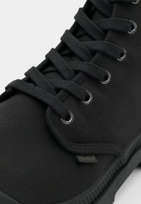 Svart lerret sneakers med teksturert overflate, rund tå og kontrastfargede snørehull. Har flate lisser og en sydd mellomsole. Merket er synlig.