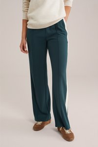 Teal wijde broek met witte zijstreep, gemaakt van een gestructureerd materiaal. Gecombineerd met bruine sneakers voor een casual uitstraling.