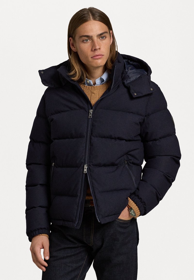 Navy puffer jacket featuring a hood, zip closures, and ribbed cuffs. Made of a smooth fabric with a quilted design for insulation.