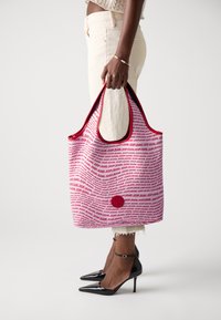 Tote torba v rdeči in beli barvi s potiskanimi besedami "JOOPJEANS." Ima trdno zasnovo, mehak material in okroglo logotipsko podrobnost na sprednji strani.