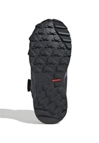 Schwarze Außensohle mit strukturiertem Muster, ausgestattet mit Traktionsnoppen und einem roten "adidas TRACTION"-Label, das sich in einer gebogenen Form zur Zehenpartie hin zieht.