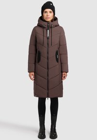 Caban maro căptușit cu glugă, având modele în formă de vopsea, buzunare laterale, fermoar lung și accente negre. Purtați cu colanți negri și cizme.