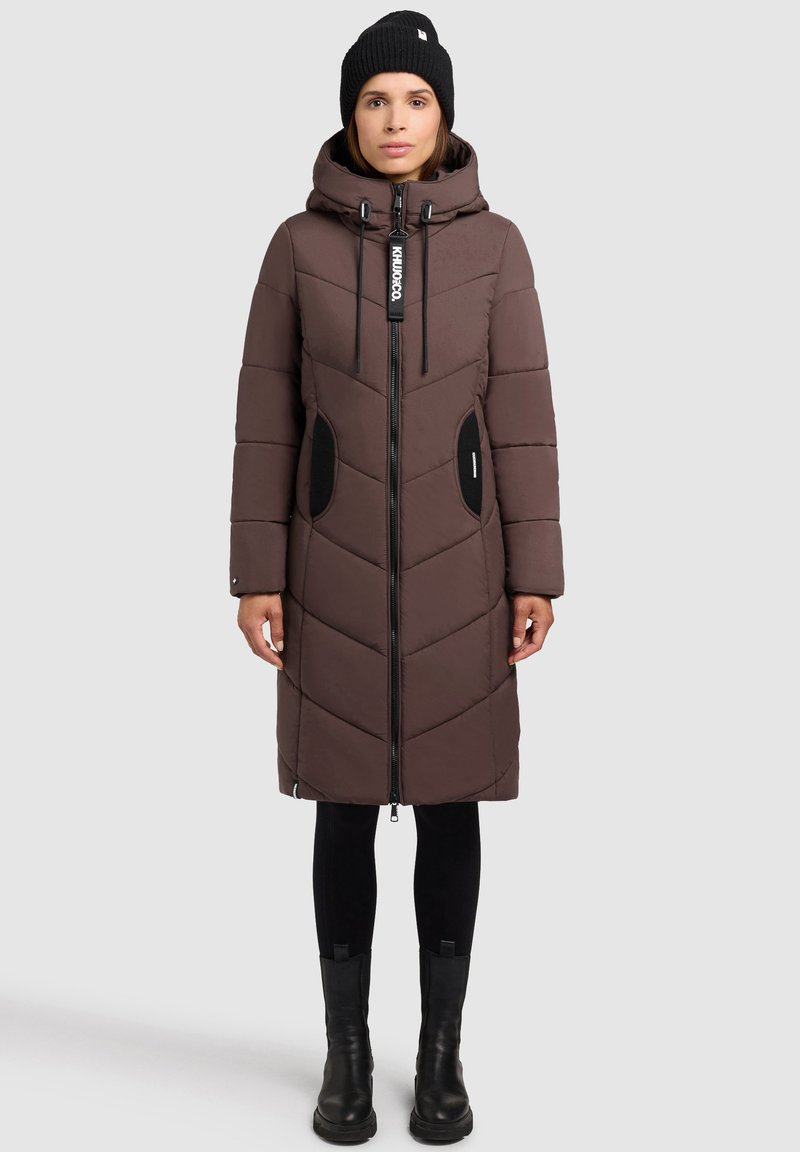 Caban maro căptușit cu glugă, având modele în formă de vopsea, buzunare laterale, fermoar lung și accente negre. Purtați cu colanți negri și cizme.