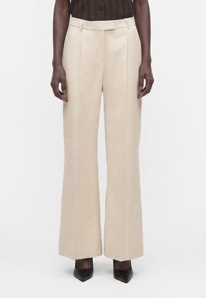 Beige broek met hoge taille en wijde pijpen, gedragen door een persoon met een donkerbruin topje en zwarte puntige schoenen.