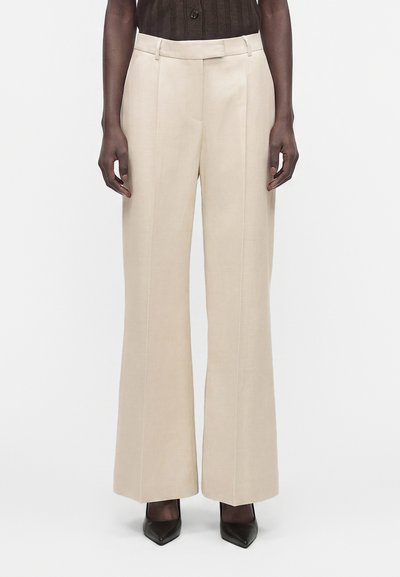 Pantalon beige taille haute à jambes larges porté par une personne avec un haut marron foncé et des chaussures pointues noires.
