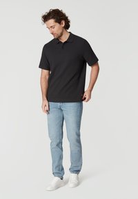 Černé polo tričko s krátkým rukávem, textura látky, dva knoflíky u límce. V páru se světle modrými džíny a bílými teniskami.