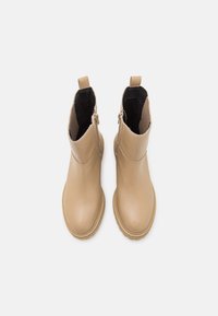 Stivaletti alla caviglia color tan con tomaia in pelle liscia, rivestimento nero, cerniere laterali e linguette per il raggiungimento. Punta rotonda con suola leggermente testurizzata.