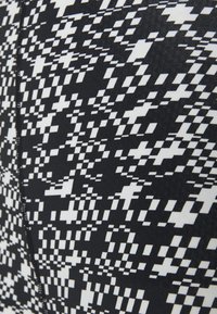 Tecido estampado em preto e branco com um design pixelizado, apresentando uma textura suave e detalhes de costura visíveis.