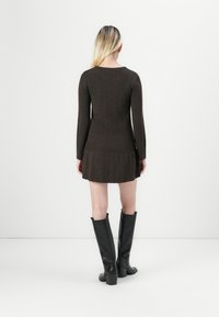Abito a maglia marrone a coste con maniche lunghe, fondo svasato, scollatura a girocollo; abbinato a stivali neri con tacco fino al ginocchio. Design minimalista.