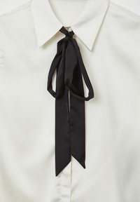 Chemise blanche à col avec un nœud papillon noir étroit et lâchement noué au cou, montrant un tissu lisse et une fermeture simple à boutons.