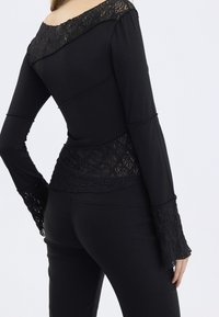 Svart långärmad topp med spetsdetaljer på axlarna och ärmarna. Figursydd design, mjuk textur och lager av spets i fållen.