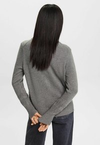 Šedý pletený svetr s kulatým výstřihem a žebrovanými manžetami. Má dlouhé rukávy, volný střih a texturovaný povrch. Nošený s tmavými džínami.