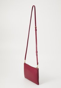 Red leather crossbody bag with a soft texture, rectangular shape, adjustable strap, and gold hardware accents. Zippered closure on top.
