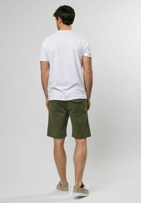Camiseta blanca de manga corta, pantalones cortos verde oliva y zapatillas beige. Diseño sencillo con un corte relajado y tejido suave.