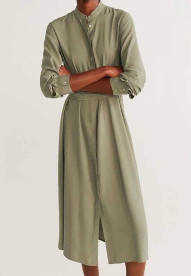 Personne portant une longue robe chemise vert olive avec des manches longues et un col montant, bras croisés devant.