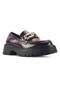 Zapato tipo mocasín de charol burdeos con un acento de cadena dorada, suela gruesa de goma negra y detalles estriados en la parte inferior.