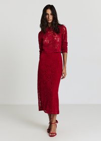 Rotes Spitzenkleid mit langen Ärmeln und figurbetonter Silhouette, versehen mit einem Blumenmuster und einem Schlitz, kombiniert mit roten Riemchenabsätzen.
