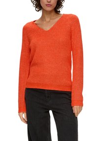 Heldere oranje sweater met v-hals, geribbelde textuur, lange mouwen en een aansluitende zoom. Gecombineerd met zwarte broek voor contrast.