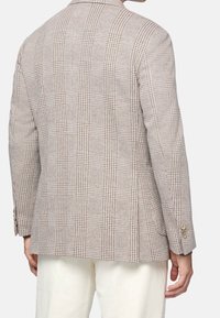 Rutig kavaj i ljusbrunt och crème, med snedkrage, strukturerade axlar och knäppta ärmar. Texturerad tyg med ett subtilt mönster.