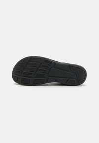 Black athletic shoe outsole featuring a textured, patterned design with flex grooves and rubber grips for traction and durability.