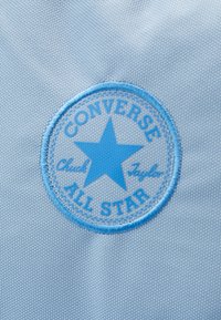 Blå Converse All Star cirkulär logotyp patch med en stjärna i mitten, sydd på ljusblå texturerad tyg.