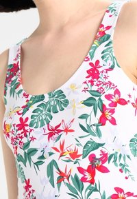 Blommig linne med vit botten och flerfärgade tropiska blommor samt gröna blad, tillverkat av lätt och stretchigt material.