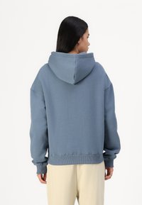 Sweatshirt azul de algodão com capuz grande, ombros caídos e punhos canelados, apresentando um corte descontraído e textura suave.