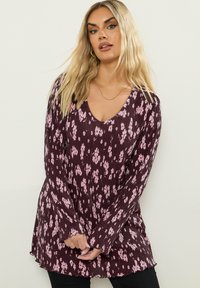 Túnica de manga larga y escote en V profundo en burdeos con un pequeño patrón floral rosa, tela texturizada y puños acampanados. El dobladillo presenta un borde con volantes.