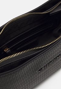 Svart strukturerad läderhandväska med gyllene dragkedja delvis öppen som avslöjar ett inre zippered fack och tygfoder.