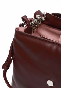 Borsa a mano in pelle color bordeaux con texture liscia, dotata di chiusura a catena d'argento, fodera rosa e un elemento rotondo in metallo argentato.