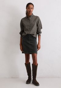 Lange mouwen overhemd met bloemenpatroon in zwart en wit, gecombineerd met een nauwsluitende donkergroene denimrok en bruine suède laarzen tot de knie.