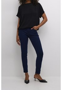 Sort kortærmet bluse, blå skinny jeans og sorte spidse stiletter med en dekorativ spænde. Enkel og moderne påklædning.