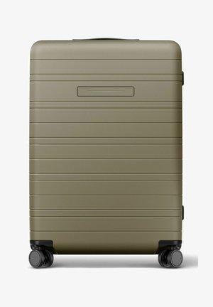 Valise rigide vert olive avec des rainures horizontales, quatre roues pivotantes noires et une poignée supérieure.