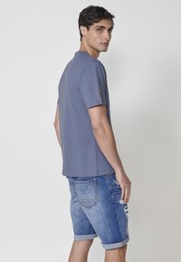 Pilkas trumpas rankovėmis marškinėliai su apvalia iškirpte. Suderinti su nusidėvėjusiais džinsiniais šortais, turinčiais suktus kraštus ir užpakalines kišenes.