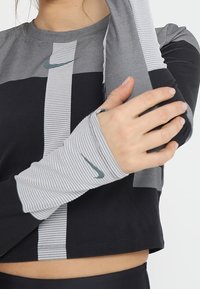 Schwarzes und graues Langarmoberteil mit einem verkürzten Design. Hat gestreifte Ärmel, einen runden Ausschnitt und ein kleines Nike-Logo auf der Brust.