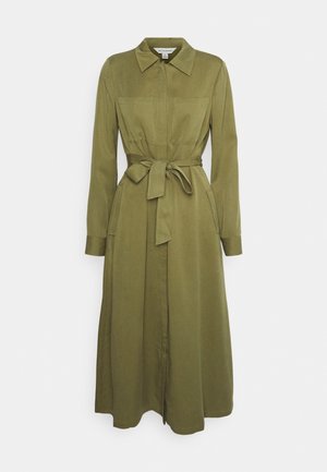 Robe chemise longue vert olive avec col, manches longues, poches poitrine, poches latérales et ceinture assortie en tissu nouée à la taille.