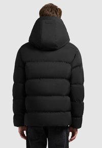 Chaqueta puffer negra con una gran capucha, diseño acolchado y costuras horizontales visibles. Textura suave y marca minimalista en la parte trasera.