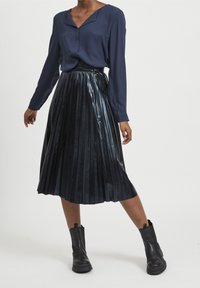 Blusa blu navy con scollatura a V, abbinata a una gonna nera a pieghe con vita alta e stivali neri alla caviglia con finitura texturizzata.