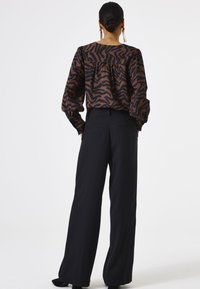 Bruine en zwarte gebloemde blouse met een losse pasvorm en ballonmouwen, gecombineerd met hoog getailleerde zwarte broek. Eenvoudig ontwerp met minimale details.